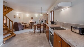 A modern kitchen with a built-in stove, a toaster, and a sink. There is a dining area with a table and chairs, and a staircase leading to an upper level. - Vamos Villa (Apokoronas)