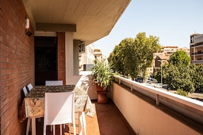 A balcony with a table and chairs, a potted plant, and a view of buildings and trees.
