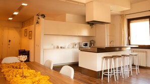 Una cucina moderna con mobili bianchi, un'isola centrale con sgabelli, un forno a microonde e un bollitore.