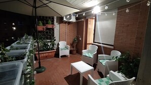 Una veranda esterna con pareti in mattoni, mobili in vimini bianco e piante in vaso.