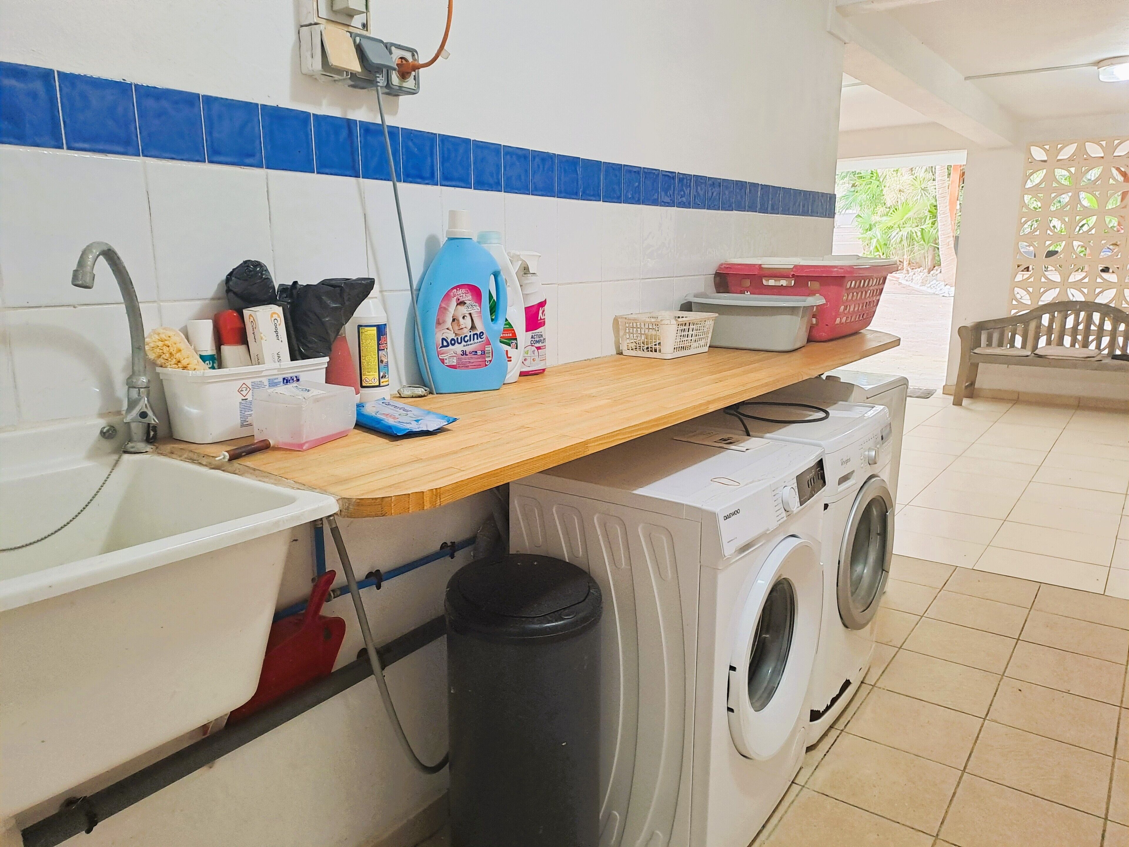 Un área de lavandería con lavadora, lavabo y mostrador con productos de limpieza.