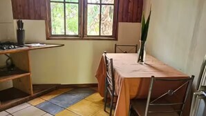 Una cocina con techo de madera, una ventana con vista a follaje, una mesa con sillas y un piso de baldosas amarillas y grises.
