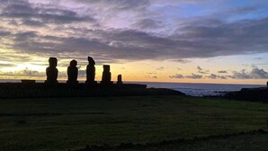 Vista al atardecer con estatuas de piedra en un campo cubierto de hierba.