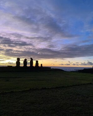 Sonnenuntergang mit Steinstatuen auf einer Wiese.