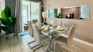 Een eetgedeelte met een glazen tafel, witte stoelen en een kamerplant.