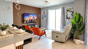 A modern living room with a flat-screen TV, a dining area with a table and chairs, and a large potted plant. - Dream Stay at Storey Lake | Heated Pool (Kissimmee)
