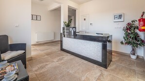 Un espace d’accueil comprenant un comptoir de réception, un coin salon avec un fauteuil en osier, une plante en pot et un extincteur.
