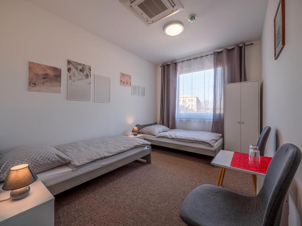 Een kleine, moderne kamer met twee enkele bedden, een bureau met stoel, een raam met gordijnen en een kledingkast.