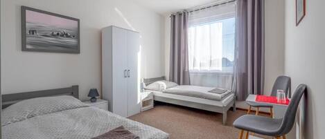 A hotel room with two beds, a desk, a chair, a wardrobe, and a window with curtains.