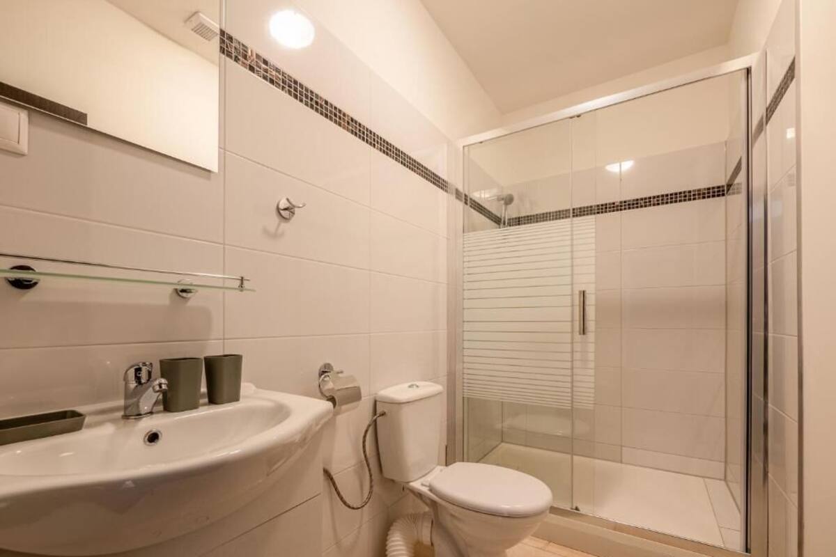 A modern bathroom with a glass-enclosed shower, a white sink with a mirror above it, and a toilet.