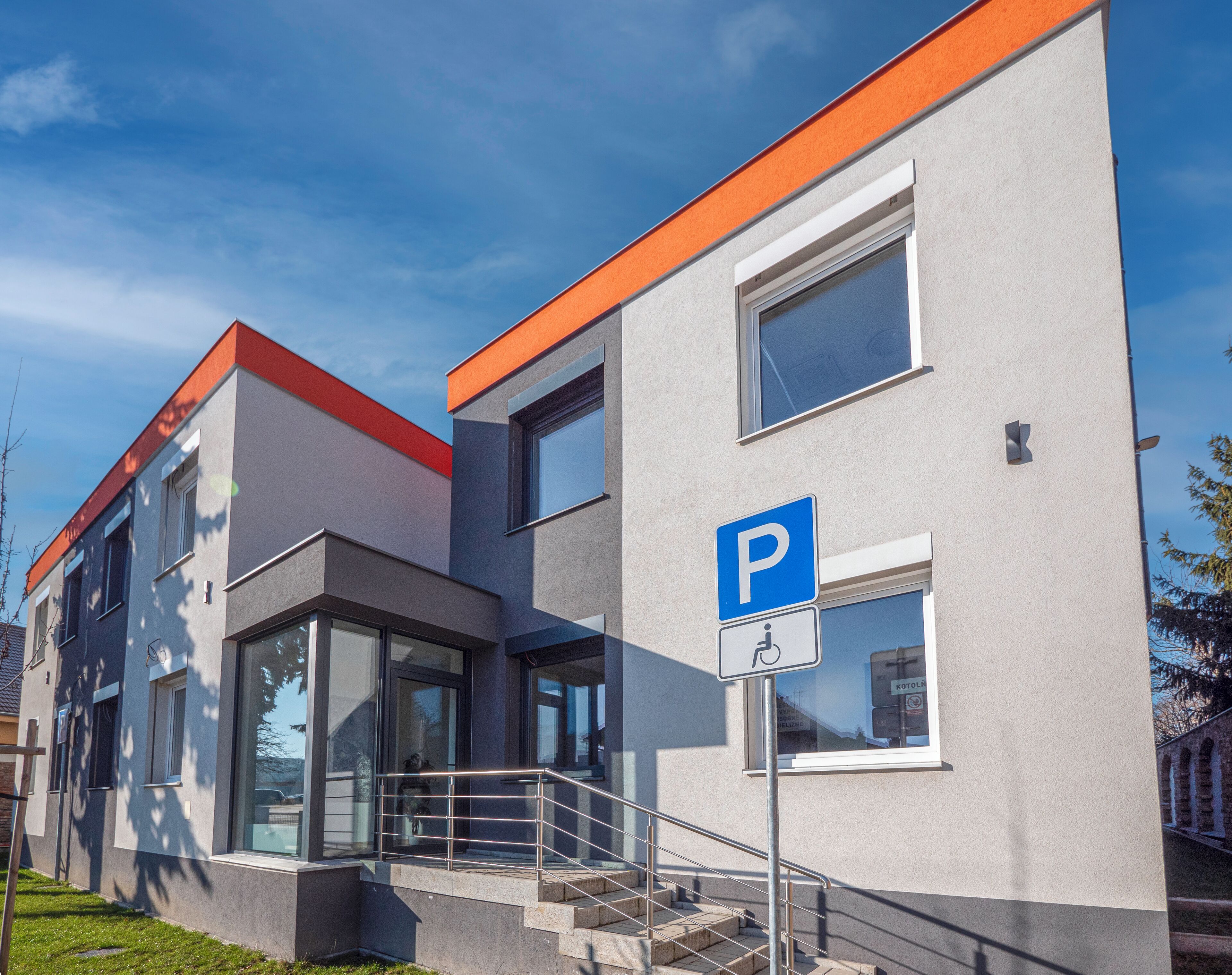 A modern building with a parking sign, a wheelchair accessibility symbol, and a staircase leading to the entrance.