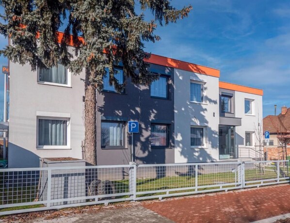 A modern two-story building with a grey facade, orange accents, and a visible parking sign. - Penzión ARIES (Nitra)