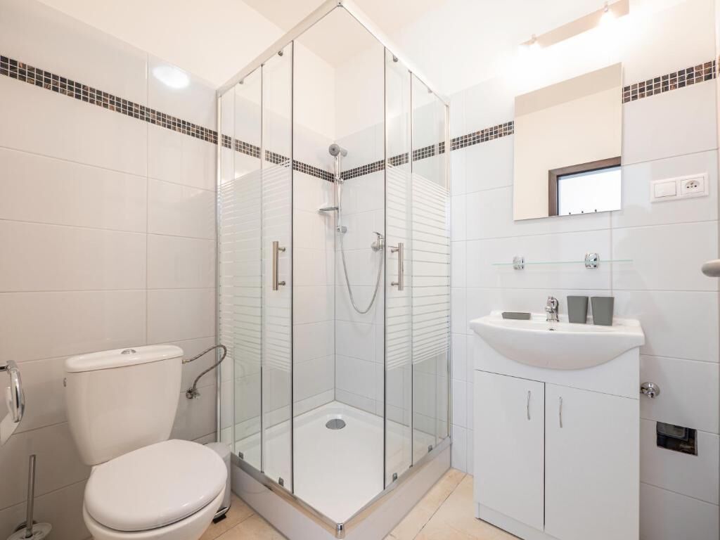 A modern bathroom with a glass-enclosed shower, a white toilet, and a sink with a mirror above it.