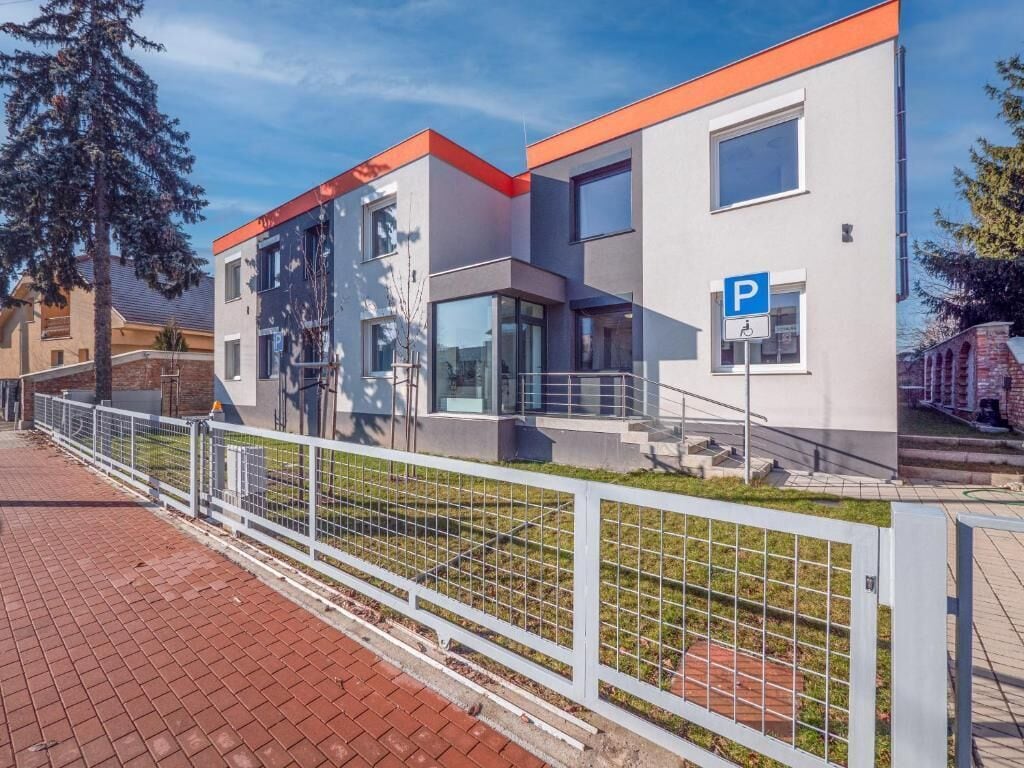 Un edificio moderno con letrero de estacionamiento, entrada protegida y un camino de ladrillo.