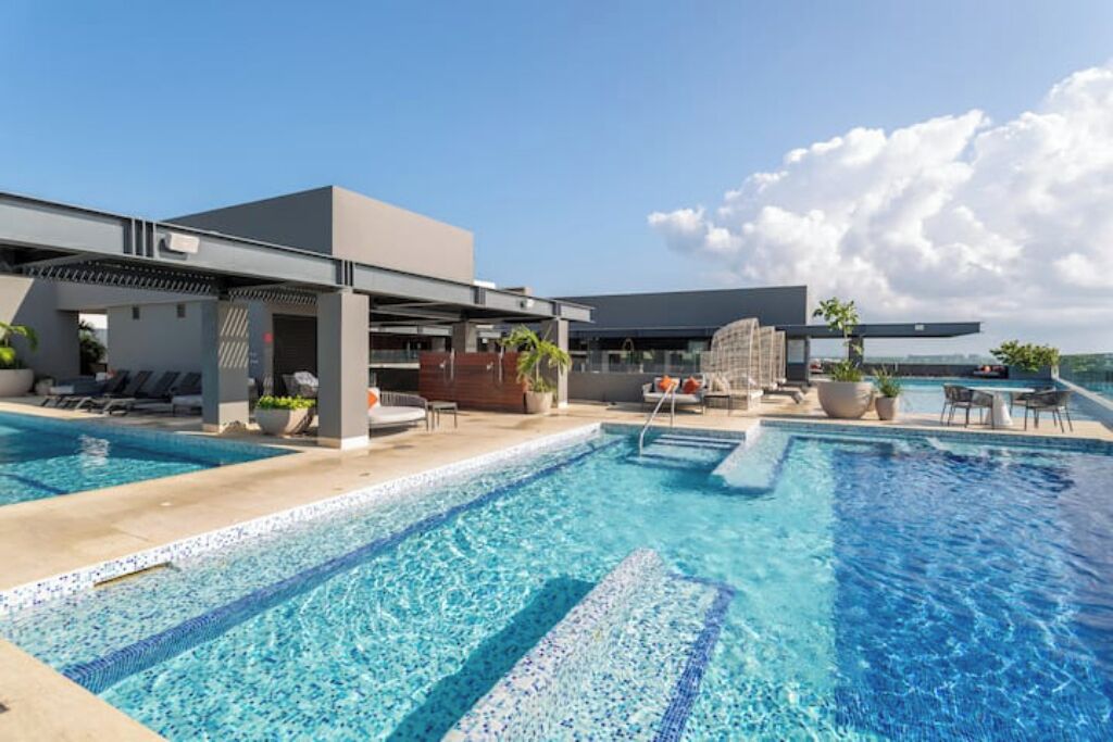 A modern hotel with a rooftop infinity pool, lounge areas, and a covered seating area.