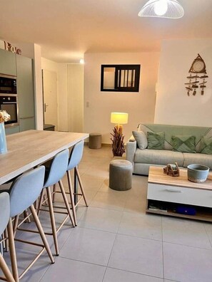 A modern living room with a wooden dining table, blue chairs, a grey sofa, and a coffee table. - Apartment in Maghjina near port and town center (Porto-Vecchio)