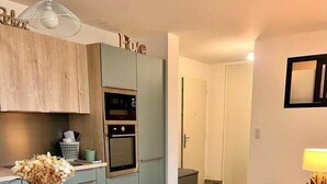 A modern kitchen with a wooden table and blue chairs, a built-in oven, and a decorative vase with dried flowers. - Apartment in Maghjina near port and town center (Porto-Vecchio)