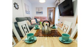 Un coin repas avec une table en bois, quatre tasses de couleur turquoise, une bouilloire et des chaises blanches.