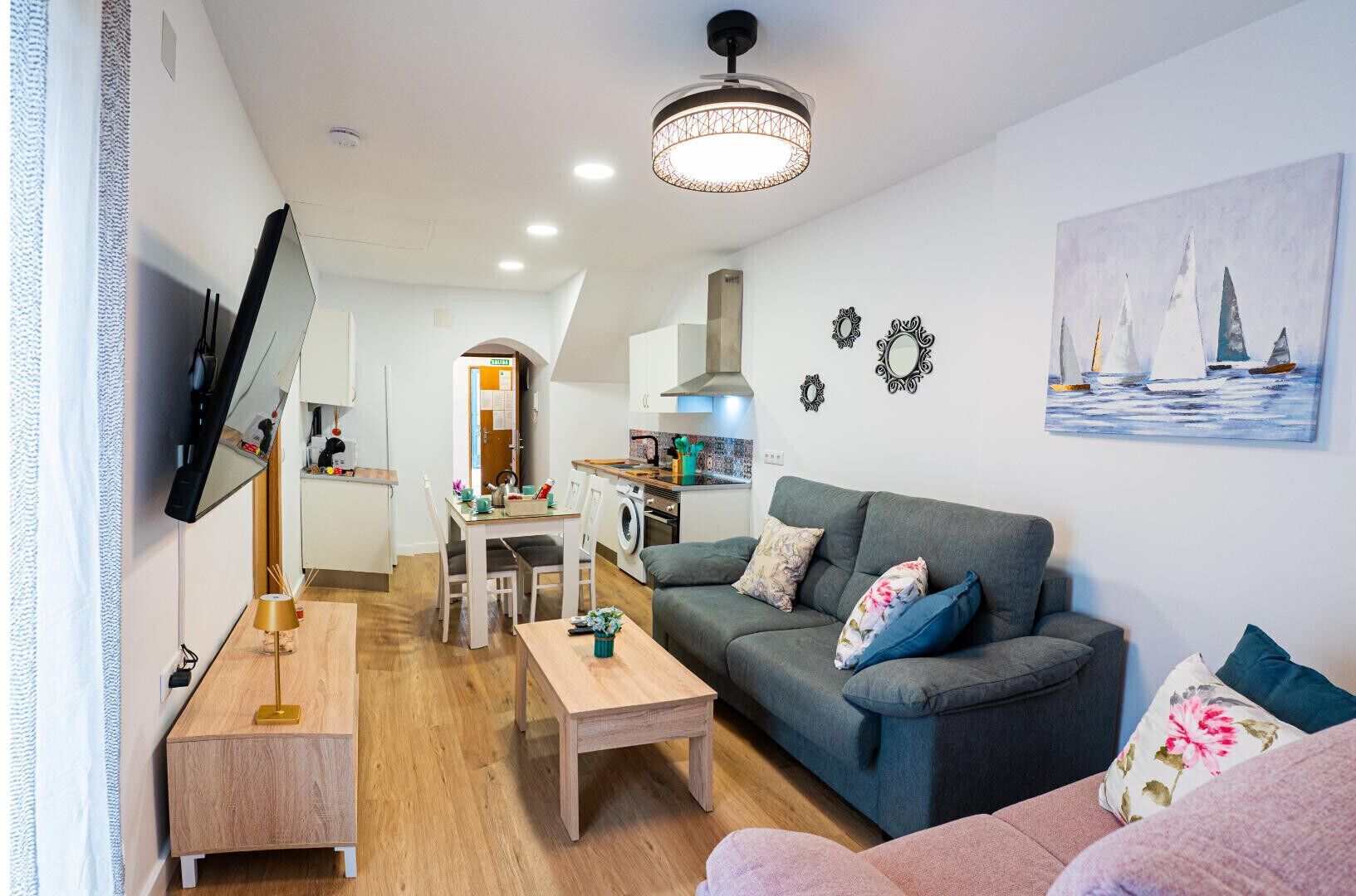 A modern living room with a grey sofa, a wooden coffee table, and a TV mounted on the wall.