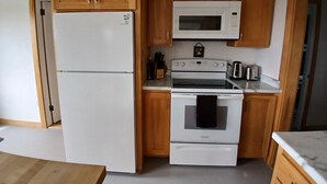 Una cocina compacta con armarios de madera, un refrigerador blanco, un microondas y un horno.