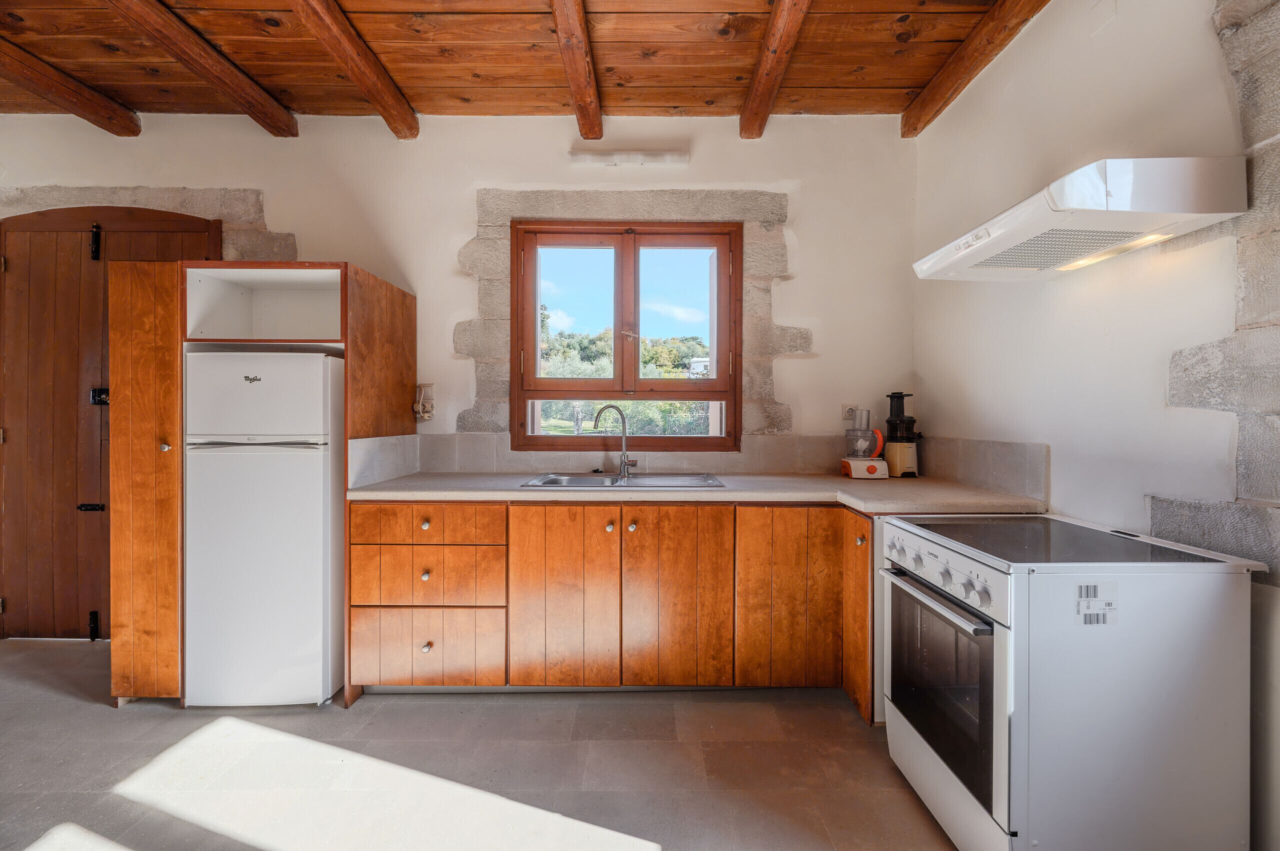 Una cocina compacta con armarios de madera, horno integrado, refrigerador y ventana con vistas al verdor.
