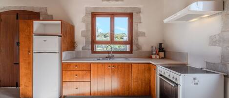 Una cocina compacta con armarios de madera, horno integrado, refrigerador y ventana con vistas al verdor.