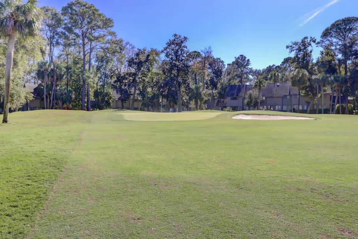 A golf course with a clear sky, trees, and a well-maintained green.