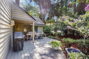 Eine überdachte Terrasse mit Tisch und Stühlen, umgeben von üppigem Grün und blühenden Pflanzen.
