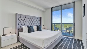 Un dormitorio moderno con una cama grande, una mesita de noche, una ventana con vistas y un balcón con sillas.