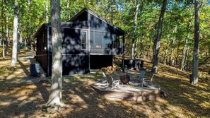 A cabin with a large deck area, a fire pit, and a covered outdoor seating area surrounded by trees. - Modern w/ Hot Tub, Grill, WiFi & Resort Access (Hedgesville)