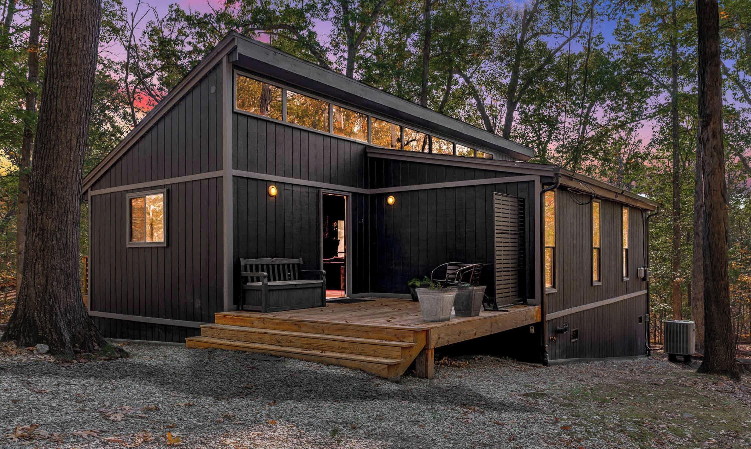 A modern cabin with a deck, large windows, and a door leading to an interior space.