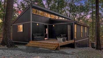 A modern cabin with a deck, large windows, and a door leading to an interior space.