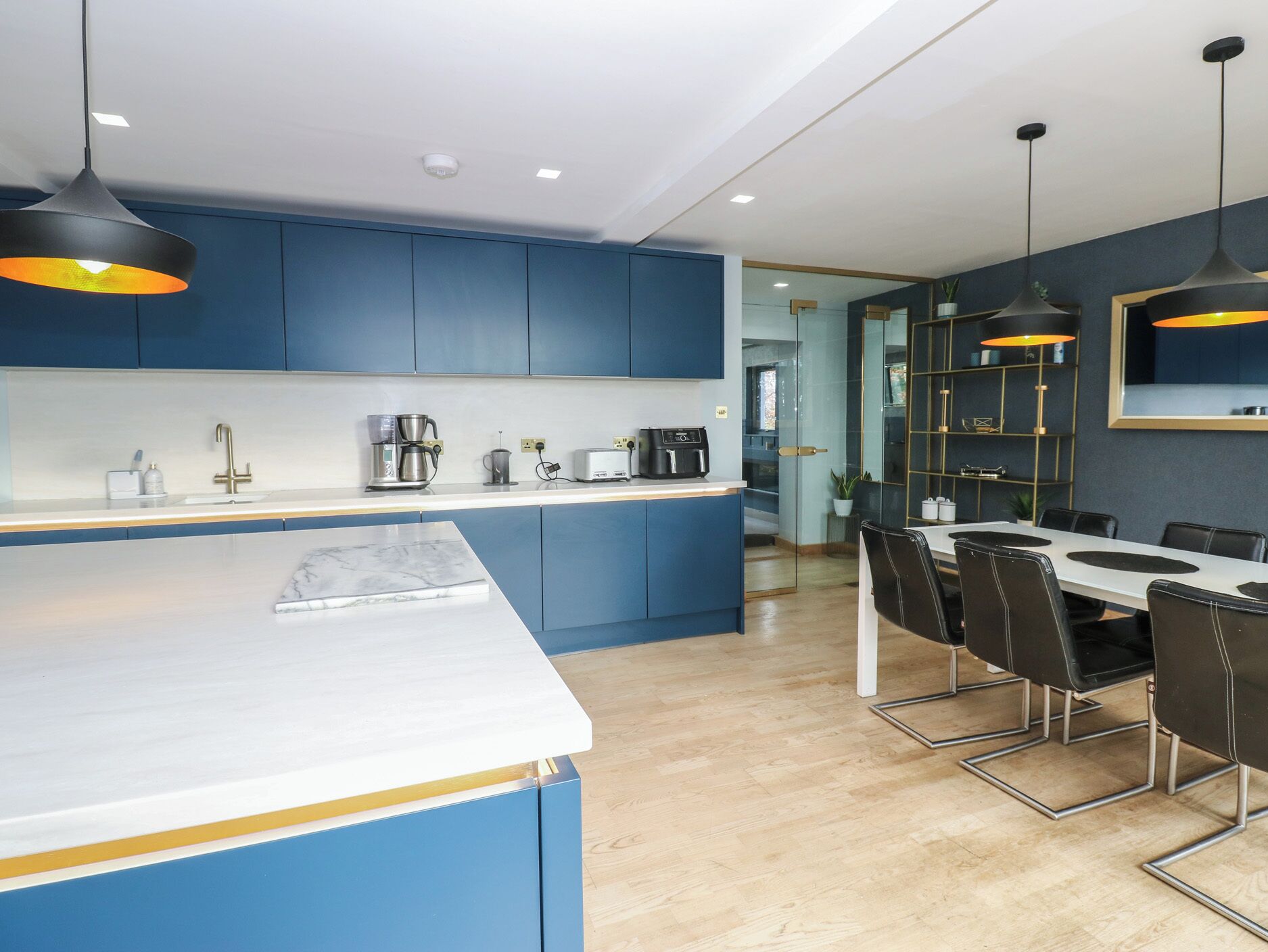 A modern kitchen with blue cabinets, a white countertop, and black pendant lights.