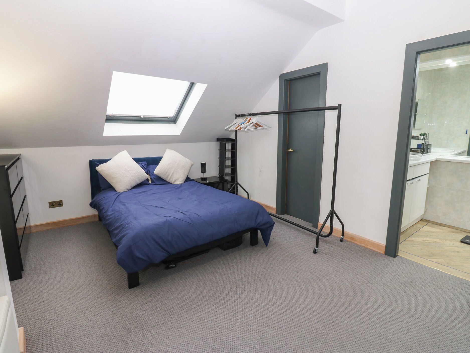 A bedroom with a skylight, a bed with blue bedding, a wardrobe, and a door leading to a bathroom.