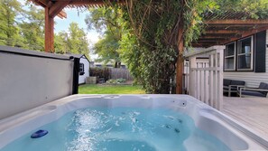 A hot tub in a backyard with a wooden deck, a white house, and a tree. - Rosewood Collective- House & Studio (Medford)