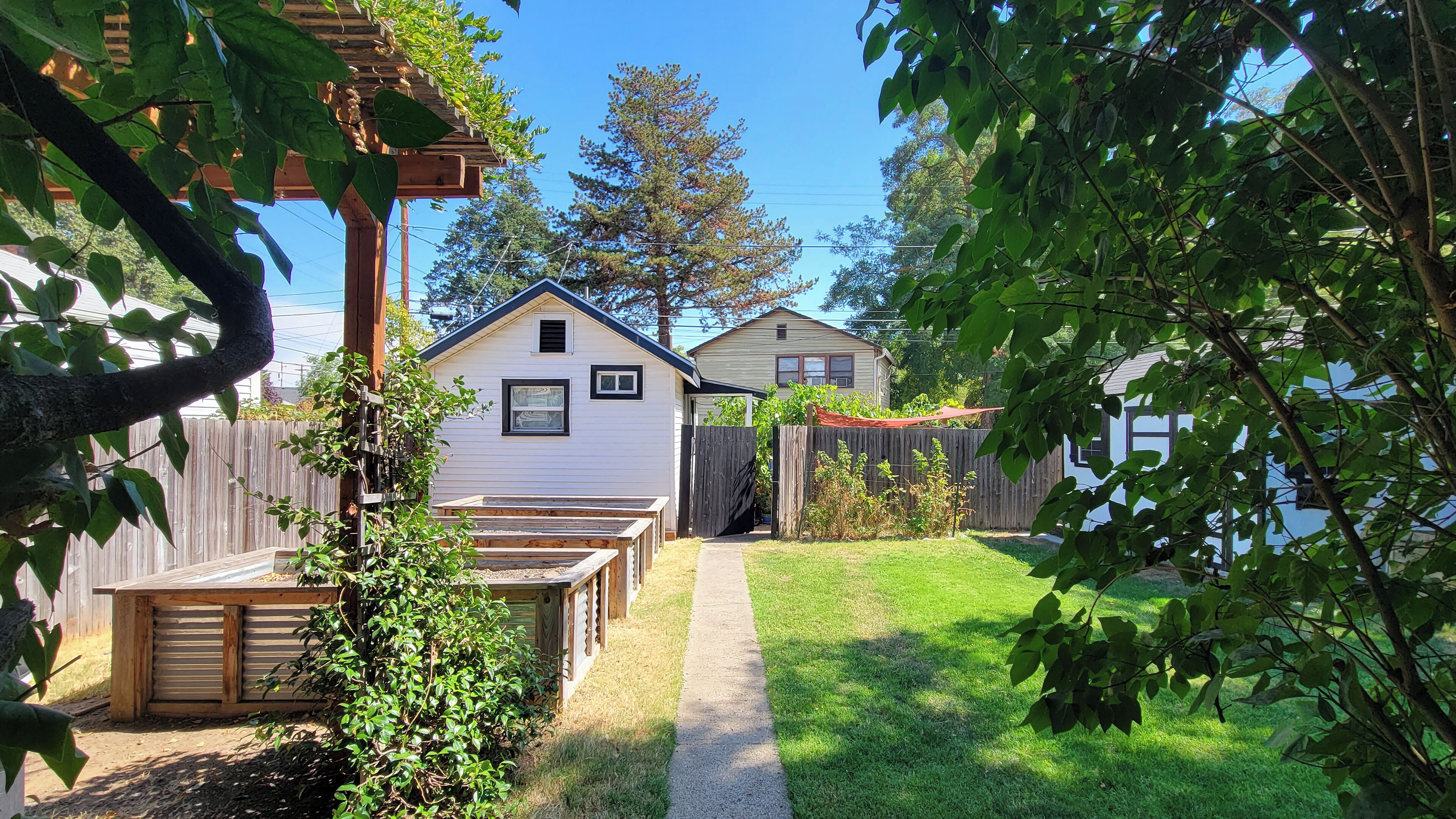 Un patio trasero con una terraza de madera, un cobertizo pequeño y un sendero que lleva a una casa.