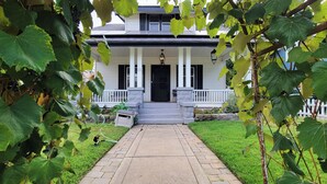 Ein zweigeschossiges Haus mit einer Veranda, einer schwarzen Tür und einem Kiesweg, der zum Eingang führt.