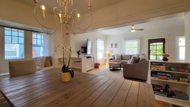 Ein geräumiges Wohnzimmer mit Holzboden, einem Esstisch, einer Couch und einem Fernseher.