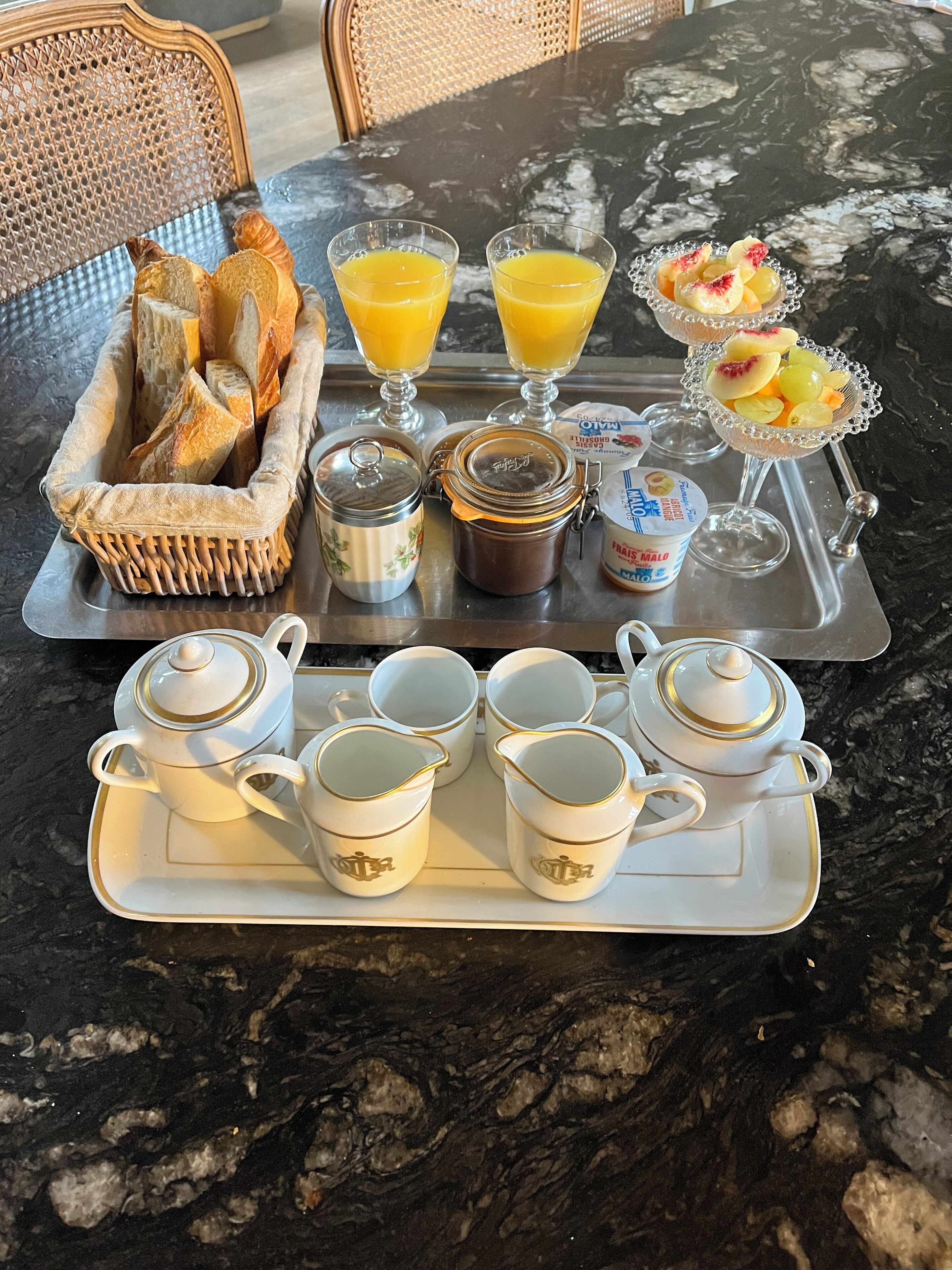 Un plateau de petit-déjeuner contenant du pain, du jus, des fruits et une théière est posé sur une table en marbre.