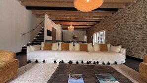 A modern living room with a sofa, coffee table, and books. There is a staircase leading to an upper level. - Domaine du Tertre ychot (Dol-de-Bretagne)