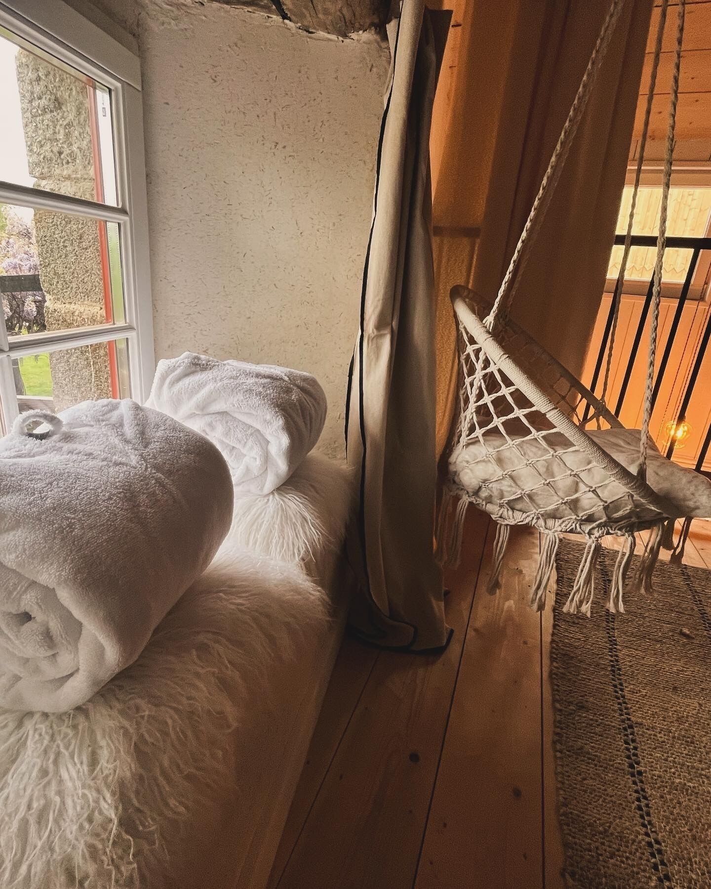 A cozy room with a bed, a hammock, and a view of the outdoors.