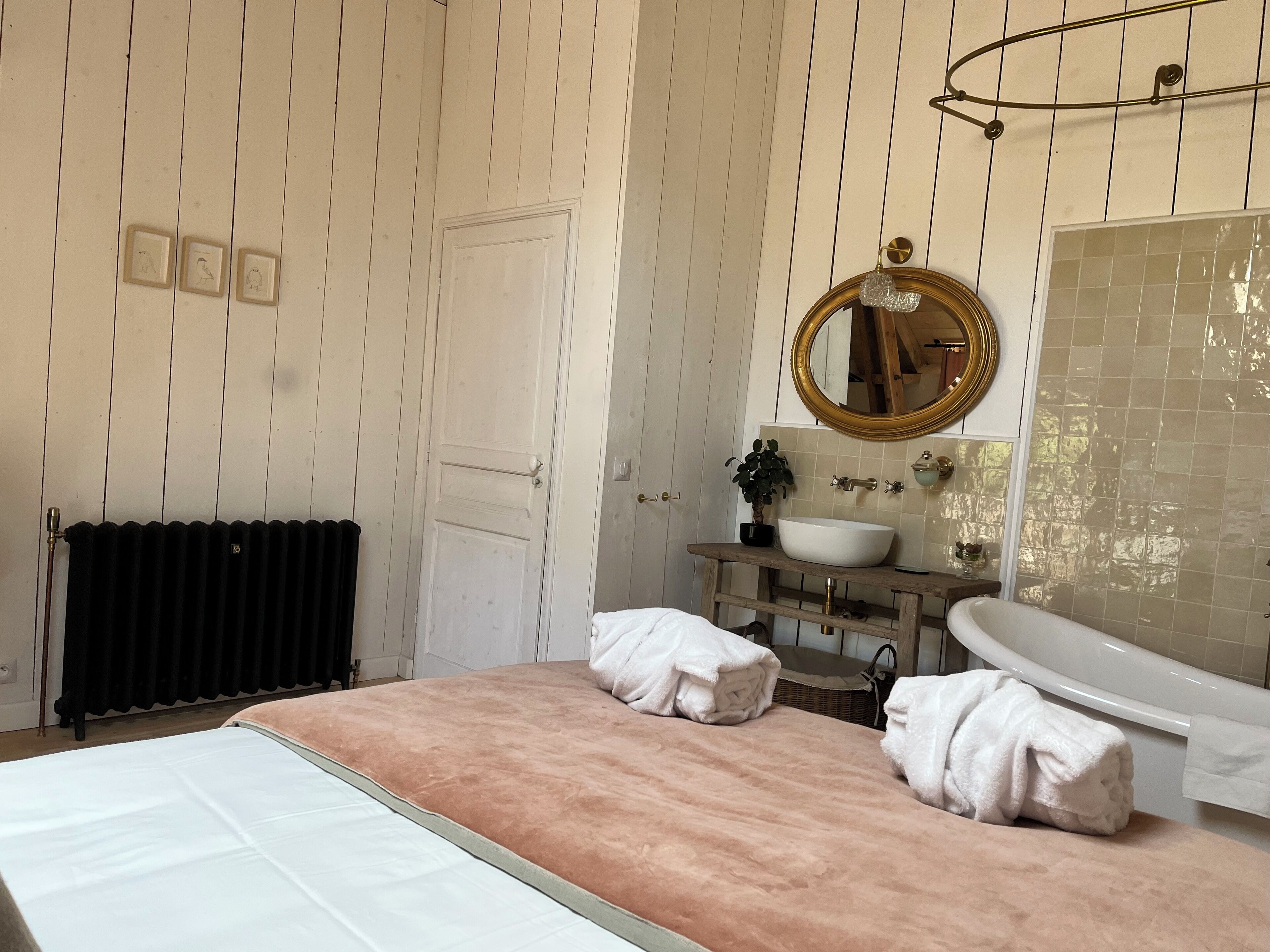 A bathroom with a white door, a wooden vanity with a sink, a mirror, and towels on the bed.