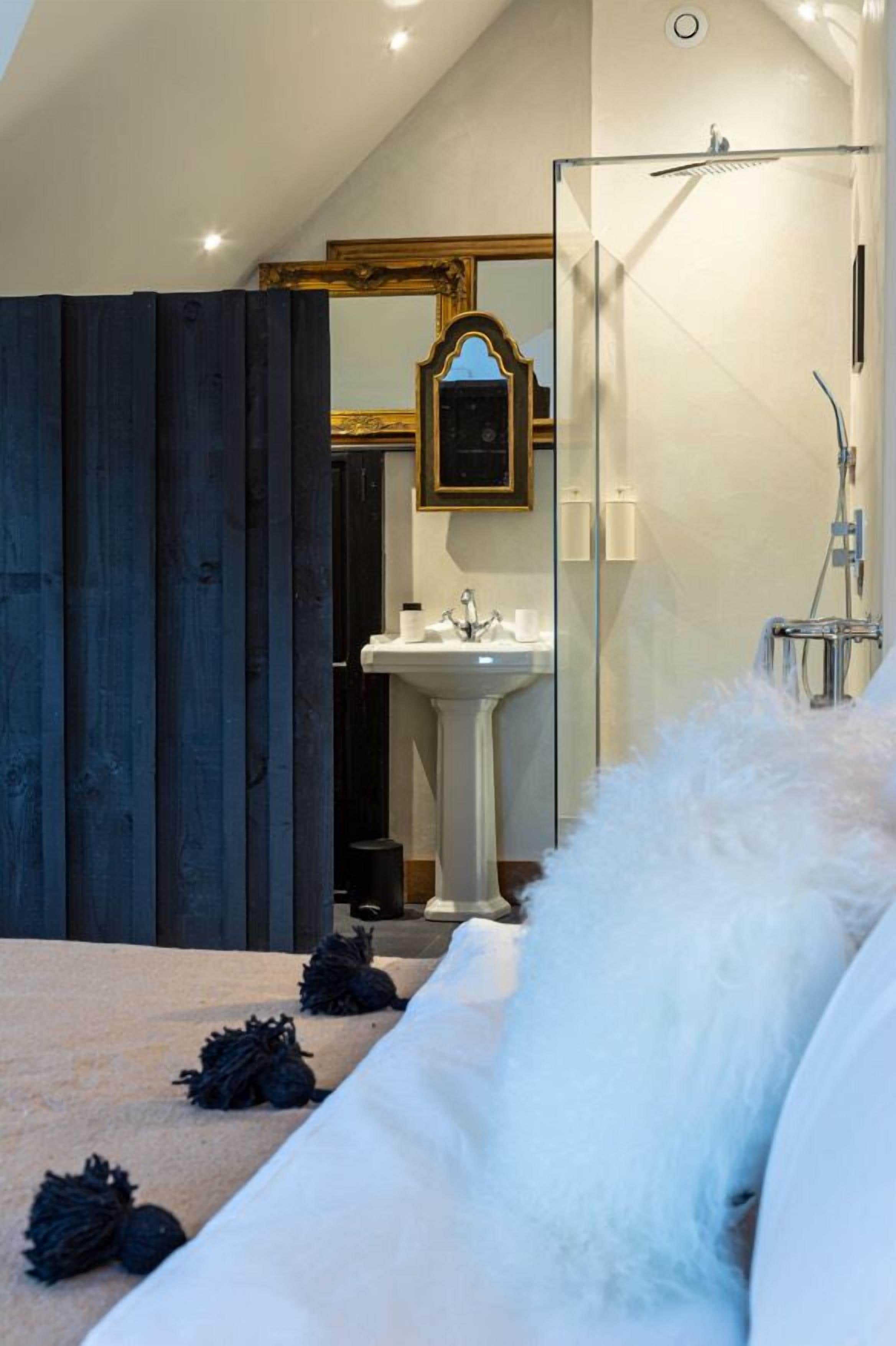 A modern bathroom with a glass shower enclosure, a white sink, and a large mirror with a gold frame.