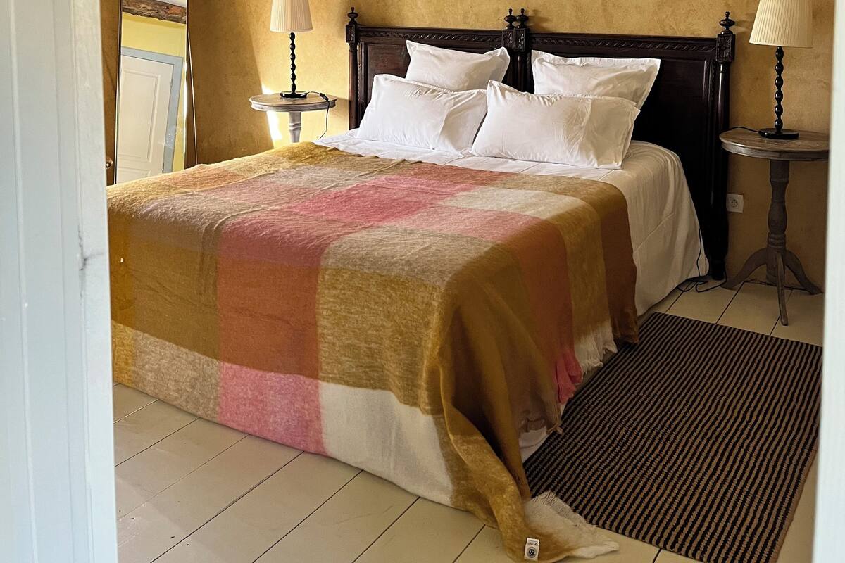 A bedroom with a sloped ceiling, a bed with white linens, two bedside lamps, and a window.