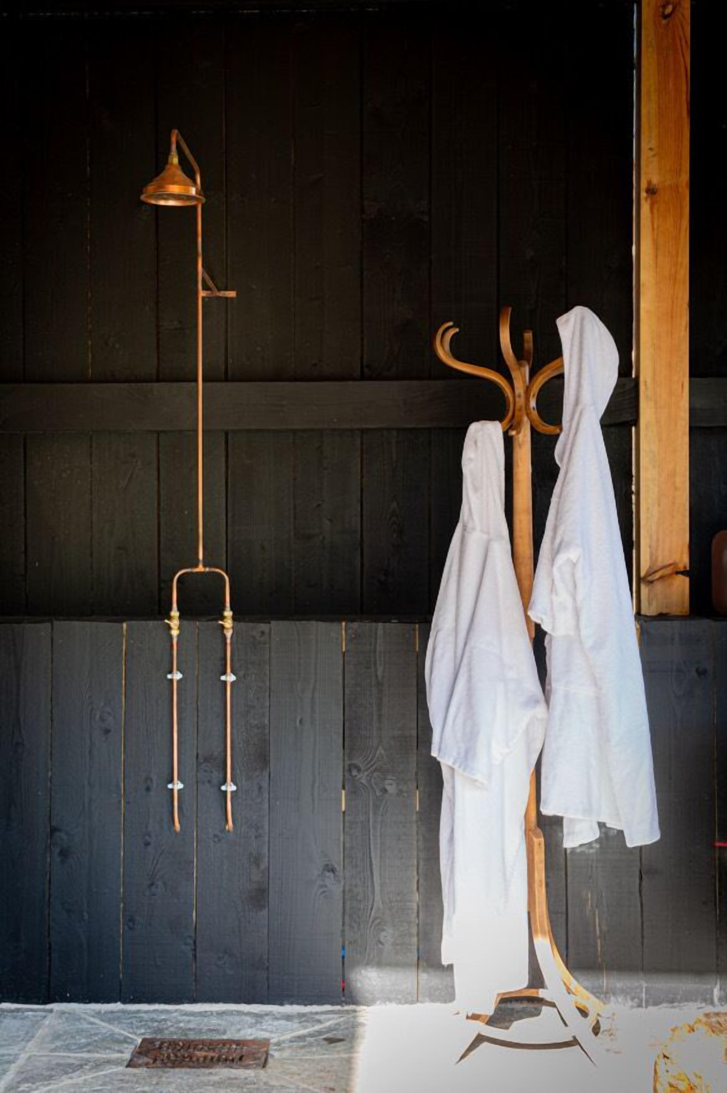 A rustic room with a wooden coat rack holding white garments, a brass floor lamp, and a wooden floor.