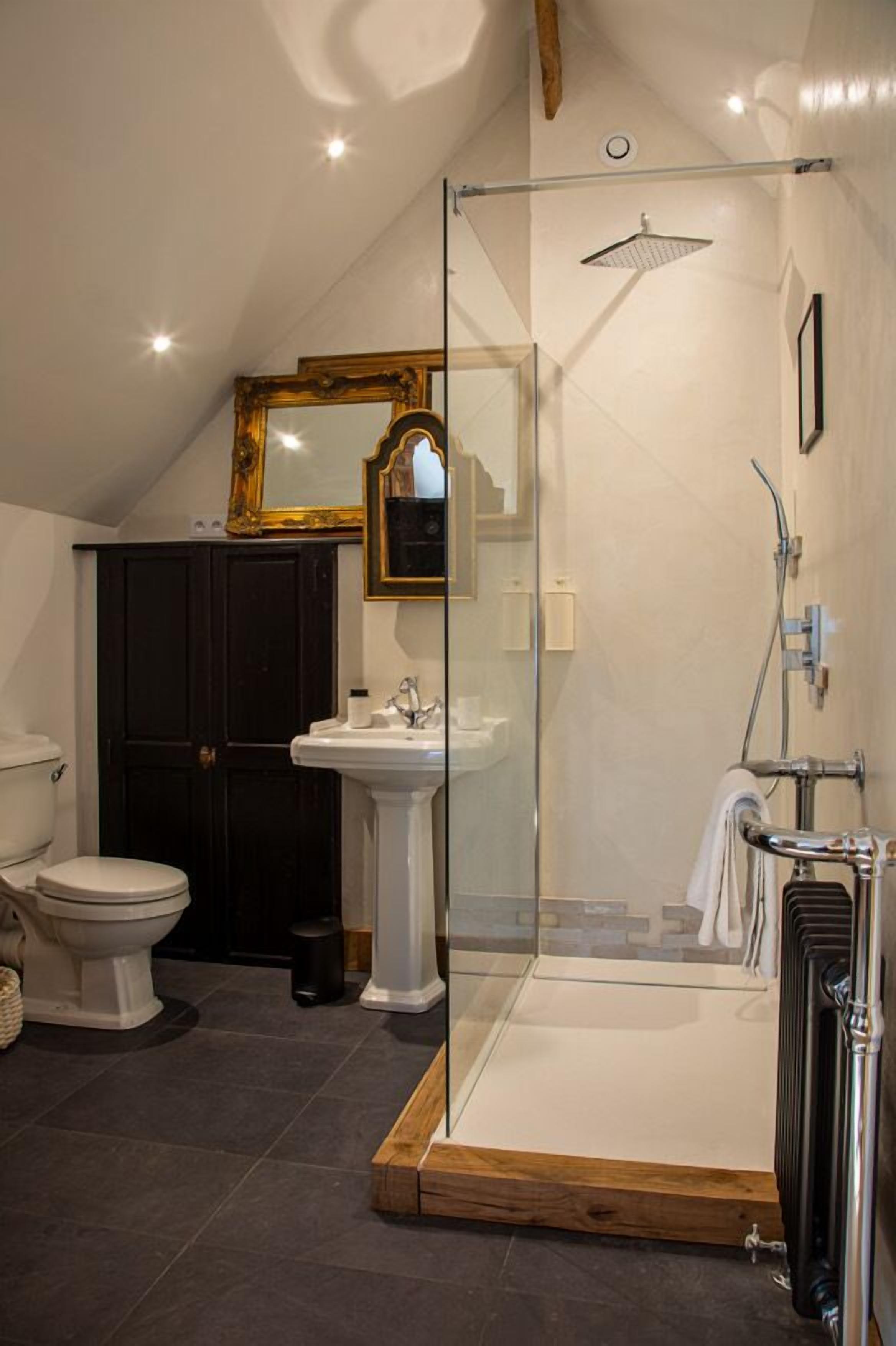 Une salle de bain avec une douche à parois de verre, un lavabo blanc, des toilettes et un meuble en bois foncé.