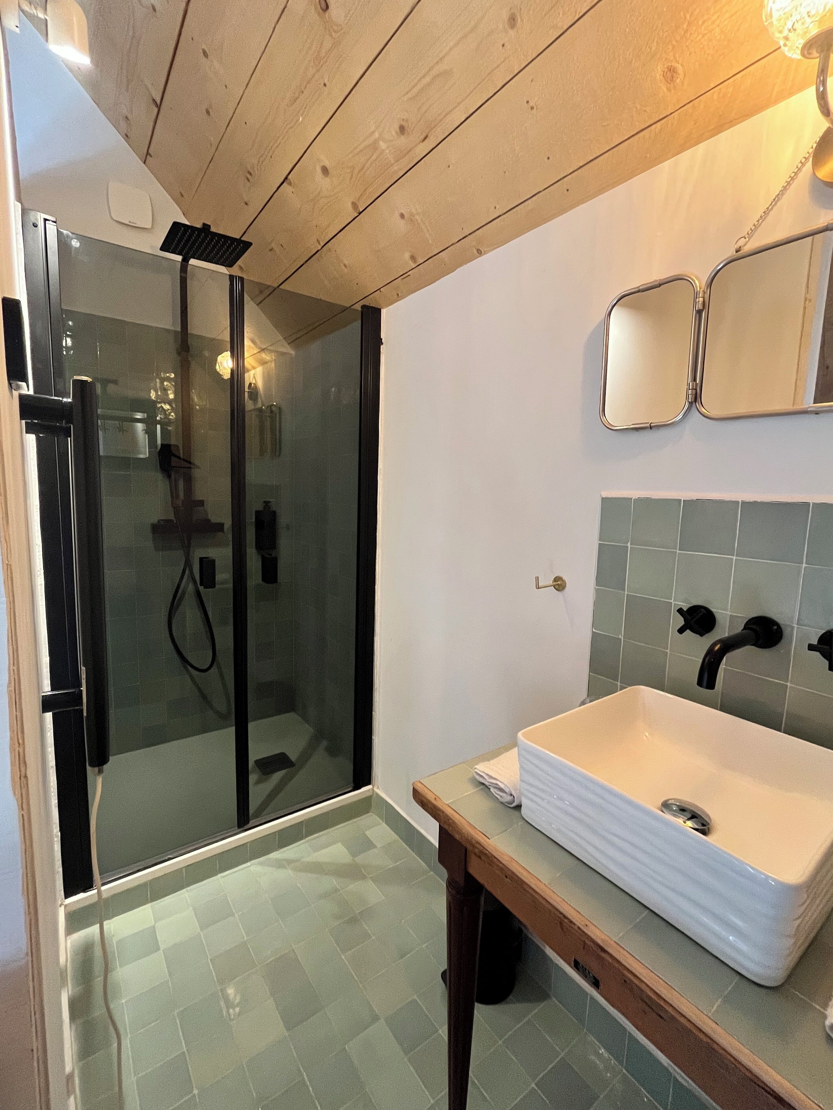 Een badkamer met een glazen douchecabine, een wit wastafelmeubel en een spiegel erboven.