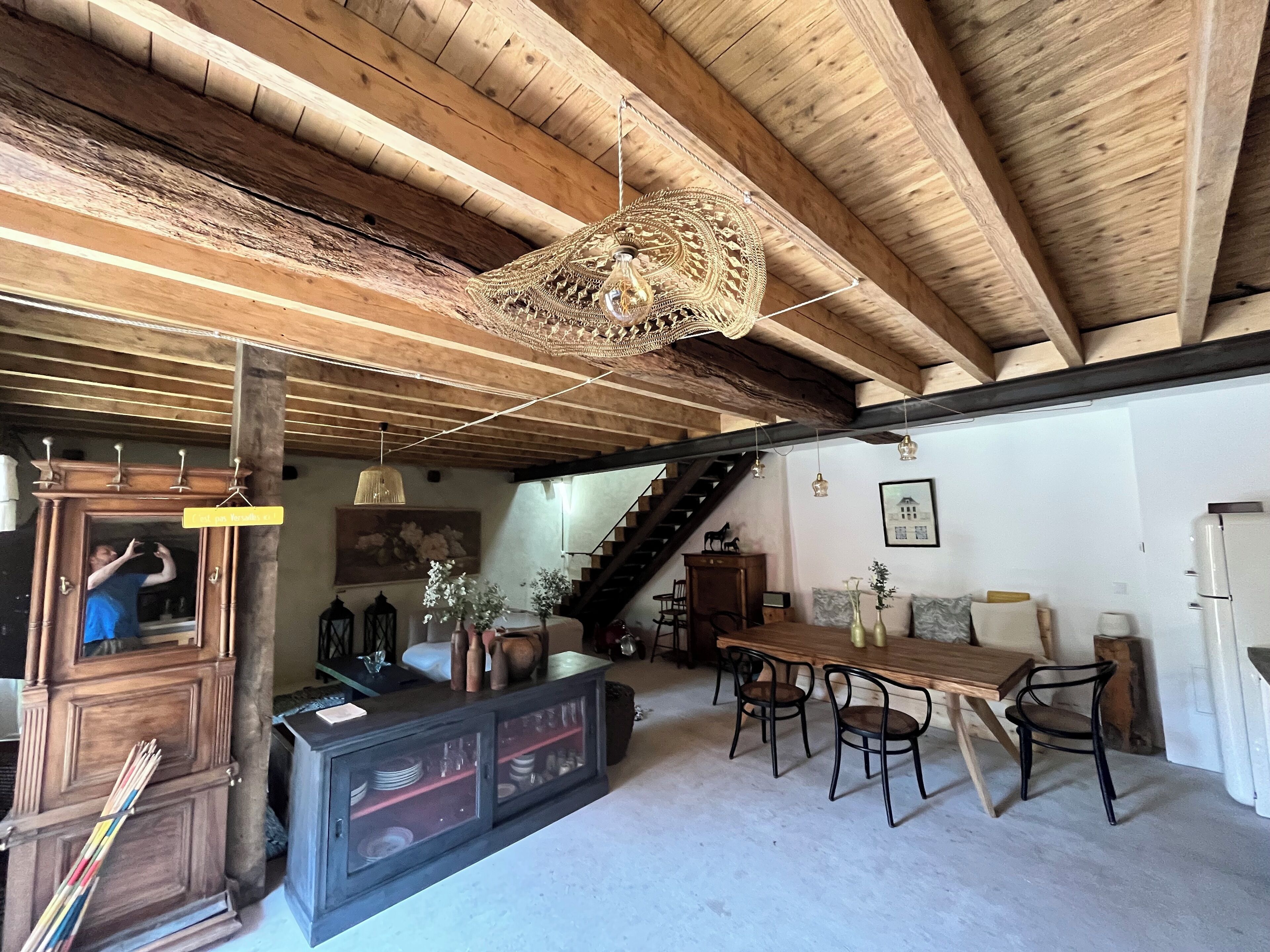 A rustic interior with a wooden staircase, a dining area with wooden chairs, and a bar area with a cabinet and glasses.