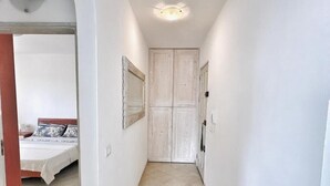Passadís estret amb un llit al fons, una porta blanca i una làmpada al sostre.