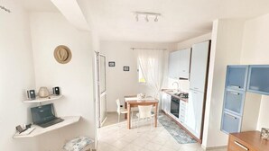 Àmplia zona d'estar amb una taula de menjador, una cuina amb armaris blaus i una petita zona de seients amb una banca i cadires.